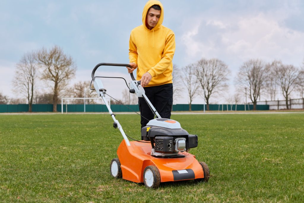 young adult male worker mowing a field with a grass cutter